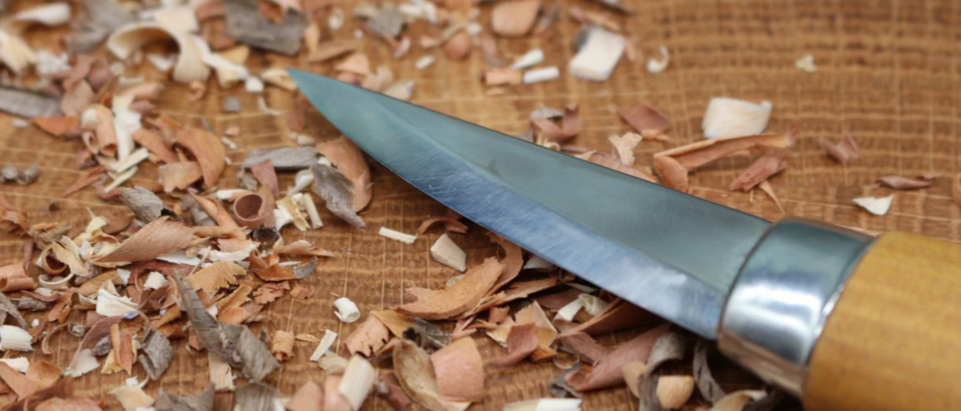 Schnitzmesser auf Werkbank zwischen Holzspänen – Detailaufnahme für präzise Handarbeit, Schnitzkunst und feine Holzarbeit aus Resthölzern