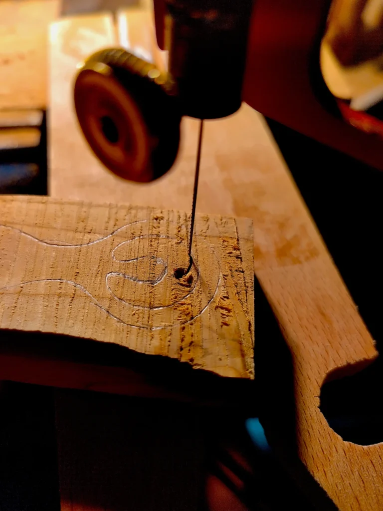 Nahaufnahme der Laubsägearbeiten an einem Göttinnen-Anhänger aus Eibenholz bei warmem Licht. Zusägen der groben Form mit einfachem Handwerkzeug.