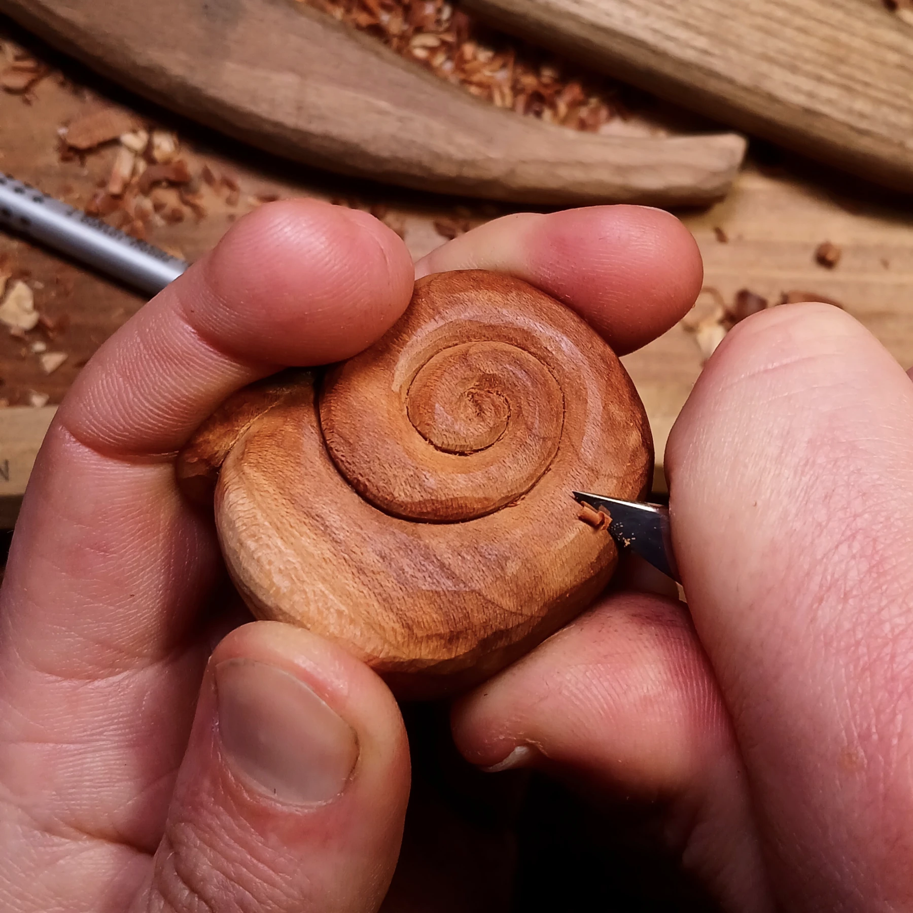 Handgeschnitztes Schneckenhaus aus Restholz in der Hand, Span wird vorsichtig mit Schnitzmesser abgenommen – handgefertigt, Naturschmuck, Waldschmuck, achtsame Handarbeit, Ruhe
